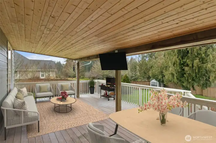 From this angle, the covered deck feels like a true extension of the home. The wood plank ceiling with two storage compartment access brings in that cozy, finished feel, while the white bannisters keep it bright and classic. There’s plenty of space for a dining table, seating, and a barbecue setup, and the mounted TV stays with the home for effortless outdoor entertaining. It’s a great vantage point over the backyard and one of those spaces you’ll use way more than you expect.