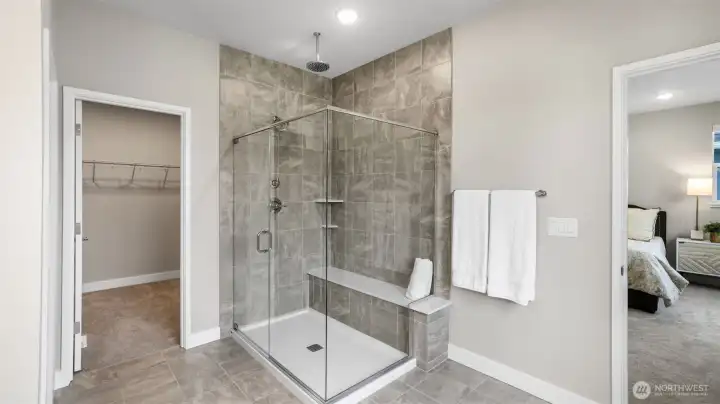 Large glass framed shower with rain dome shower head, in-shower seat, tile accents, and spacious walk-in closet