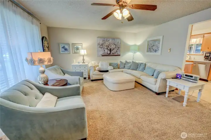 Living room with ceiling fan, large picture window flooding space with light, flooring is wall-to-wall carpet