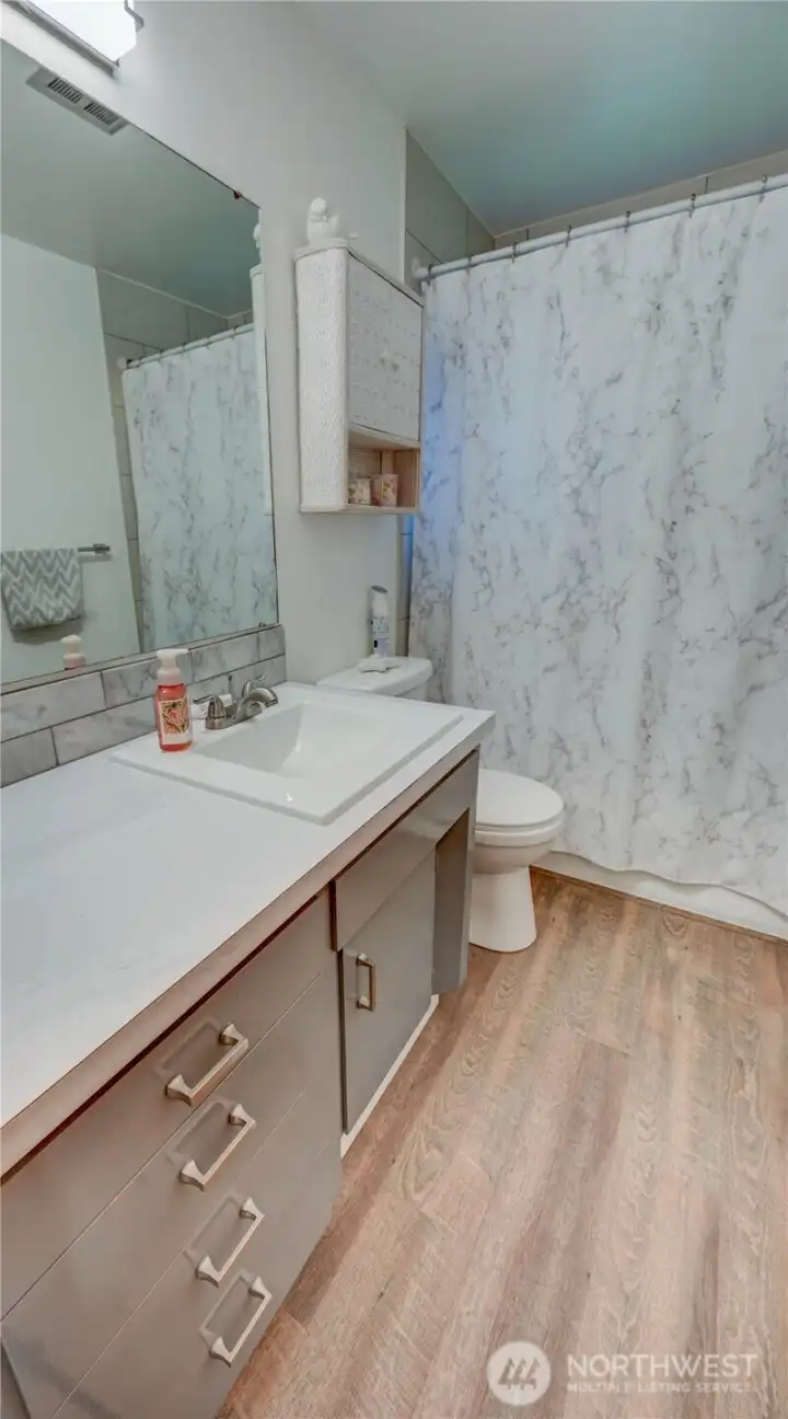 Updated full bathroom with LVP flooring, tiled shower, a vanity offering modern line sink and plenty of storage and counter space.