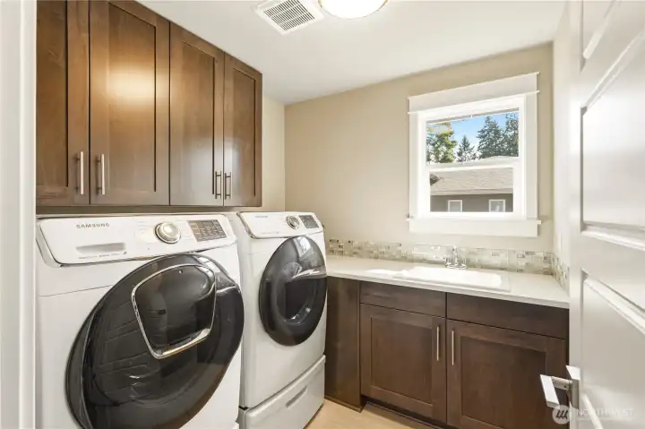 A spacious laundry room with ample storage, a folding counter, and sink.