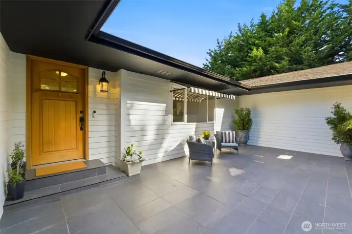 The tiled patio and awning extend the home's living space outdoors, offering a comfortable setting for dining, entertaining, and enjoying the privacy of the beautifully landscaped grounds.
