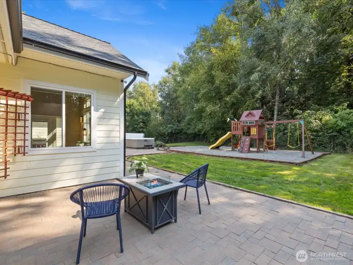 Around the corner from the main patio, a second paved area features a fun playset surrounded by a green safety barrier, creating a perfect space for kids to play.
