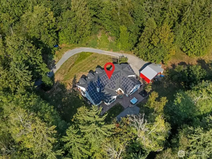 The aerial view highlights the extensive solar panels on the property, while the red building serves as the 40x20 overflow parking or equipment carport.