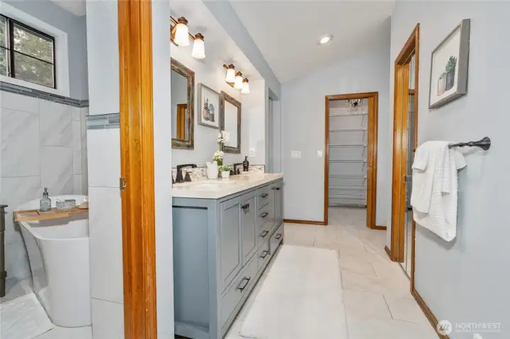 Beautifully remodeled primary bathroom looking toward the sink and another walk-in closet and the free-standing soaking tub.