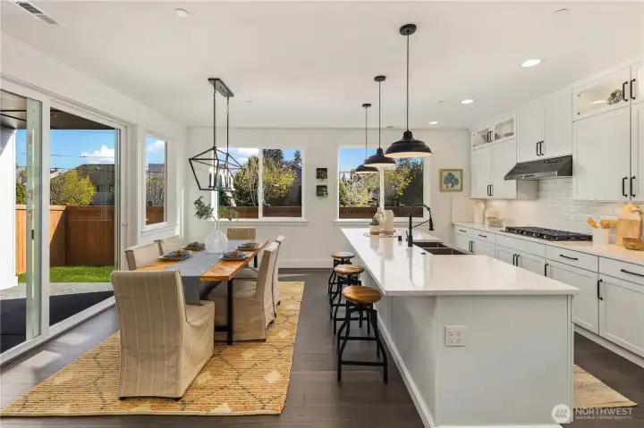 Kitchen & Dining  This connected kitchen and dining space highlights the seamless main-level layout central to modern Pacific Northwest design. A quartz island with bar seating anchors the kitchen, complemented by full-height cabinetry, a gas cooktop, wall oven, and under-cabinet lighting. Expansive windows and a sliding glass door create an easy transition to outdoor living while filling the space with natural light.    Located in Bothell’s Canyon Park neighborhood, this open living area reflects the quality and finish expected in luxury new construction within the Northshore School District.    These photos are from a past Robinson Plan at a different community, so overall plan, colors, building orientation, finishes, home outlook, and other details can and WILL vary. All photos, renderings, site maps, and floorplans are for visualization purposes only.
