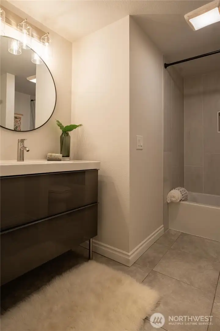 Main level full bath with tub, tile surround, tile flooring and contemporary vanity