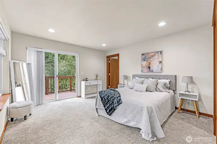 Spacious primary suite located at the back of the home, featuring large windows and a sliding glass door that opens to a private deck overlooking the surrounding trees and Lake Louise area.