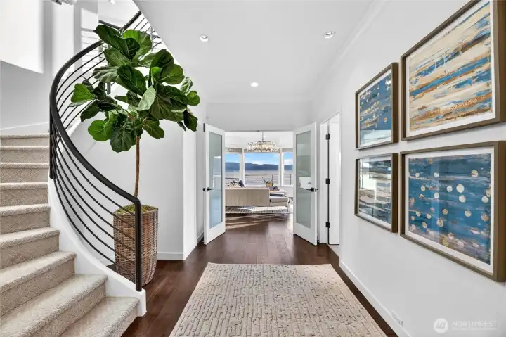 From the moment you arrive, the home makes a statement. A sculptural curved staircase and a sun-drenched gallery hall set the stage, with shimmering lake views waiting just beyond the French doors.
