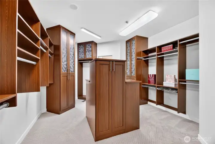 A room-sized walk-in closet with an island dresser, etched glass upper cabinets, and a pull-out tie rack — every detail considered.