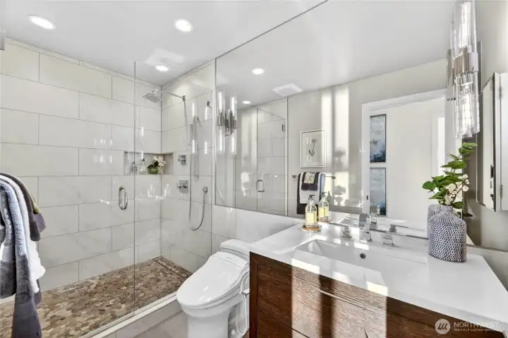 Crisp, clean, and beautifully finished, the upper level bath features a frameless glass shower with marble-look tile, pebble floor, and bidet.