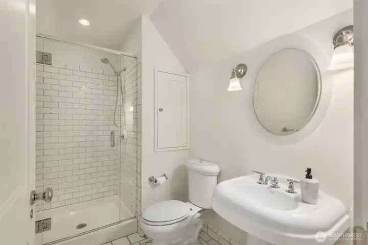 Bright bath featuring a glass-enclosed shower and a round mirror. Bright bath featuring a glass-enclosed shower and a round mirror.