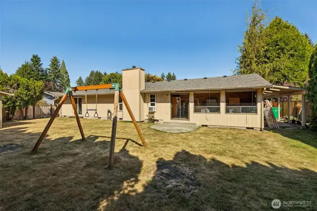 Backyard view shows patio off of the sunroom space and to the right of the house there is a great covered paved area.