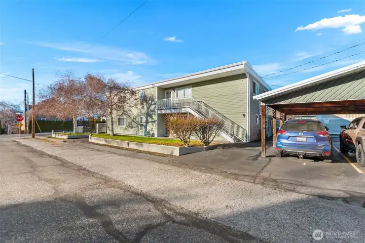 The blue car is parked in Unit #1's reserved spot under the carport, and the door to Unit 1 is just under the stairs.