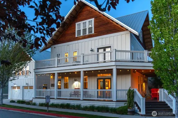 Exterior twilight view of home with classic covered wraparound porch and upper level lake view decks.