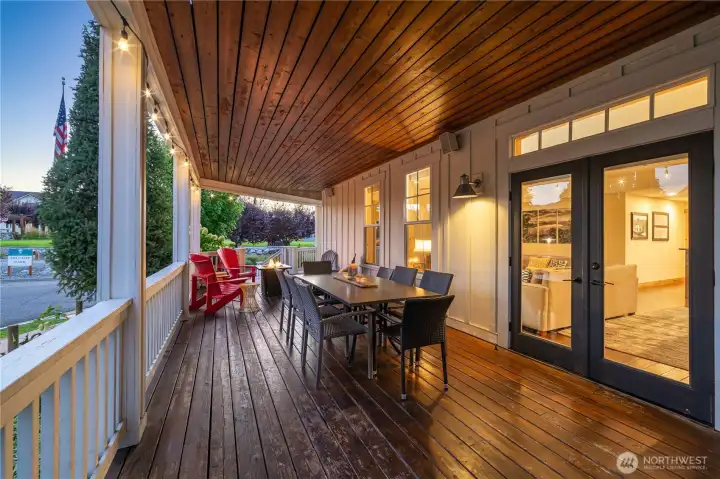 Twilight view of classic covered wraparound porch with outdoor dining, BBQ, lounge area and fire pit.