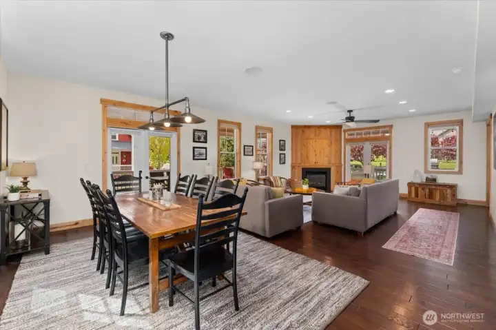 View of main level dining room and living room with French doors leading to the covered wraparound porch and outdoor living space with dining table, BBQ, lounge area and outdoor fire pit.