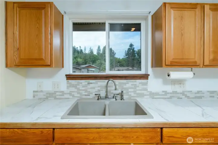 This bright kitchen features a double sink set beneath a wide window that frames peaceful views of the surrounding trees and neighborhood.