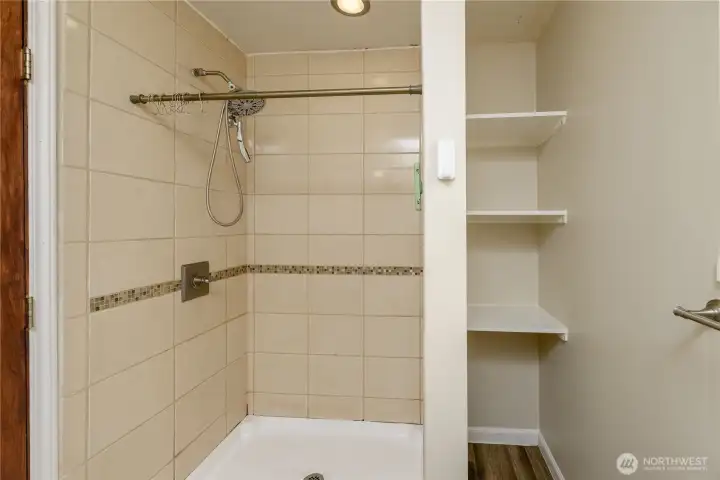 The walk-in tiled shower showcases a decorative mosaic accent strip and a rainfall-style showerhead. Built-in shelving provides convenient storage, while a frosted window brings in natural light while maintaining privacy. A comfortable and functional feature within the primary suite.