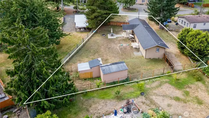 Aerial angle highlighting the backyard and outdoor living area. The property includes a patio, storage sheds, chicken coop and open yard space framed by fencing and trees, creating a versatile outdoor retreat.