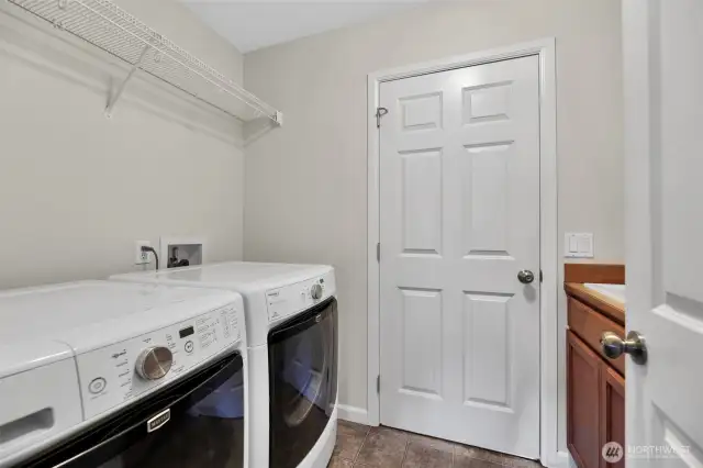 Laundry room with sink and shelving for storage. Door leads to attached 3 car garage.