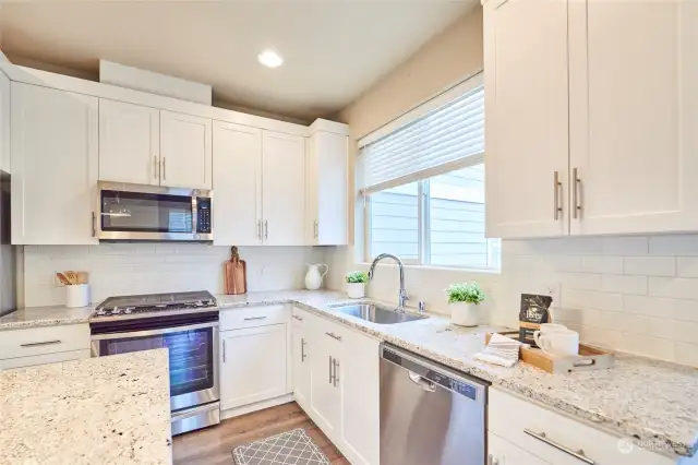 The modern kitchen complete with undermount sink, 5 burner gas stove, stainless steel appliances and a kitchen island.