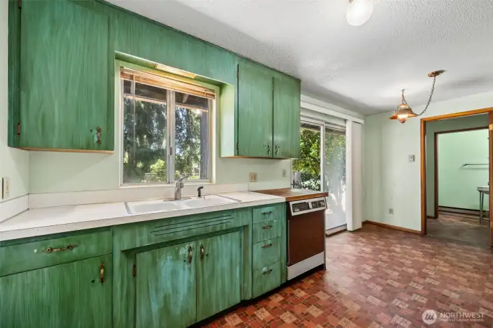 Now we're stepping into the kitchen, where vintage enthusiasts and visionaries alike may find themselves getting a little excited. Original wood cabinetry still appears to be in place awaiting to be stripped back down to it’s original finish, complete with the groovy hardware that gives so many mid-century kitchens their charm and personality. A large window above the sink overlooks the backyard, bringing in natural light while making dish duty a little more pleasant. The layout offers a comfortable blend of workspace and casual dining, with easy access to the sliding glass door and adjoining living areas. A laminate countertop, dishwasher and butcher block work surface provide a starting point for whatever comes next, whether that's a careful restoration of the home's original character or a full-scale transformation into your dream kitchen. Now we're stepping into the kitchen, where vintage enthusiasts and visionaries alike may find themselves getting a little excited. Original wood cabinetry still appears to be in place awaiting to be stripped back down to it’s original finish, complete with the groovy hardware that gives so many mid-century kitchens their charm and personality. A large window above the sink overlooks the backyard, bringing in natural light while making dish duty a little more pleasant. The layout offers a comfortable blend of workspace and casual dining, with easy access to the sliding glass door and adjoining living areas. A laminate countertop, dishwasher and butcher block work surface provide a starting point for whatever comes next, whether that's a careful restoration of the home's original character or a full-scale transformation into your dream kitchen.