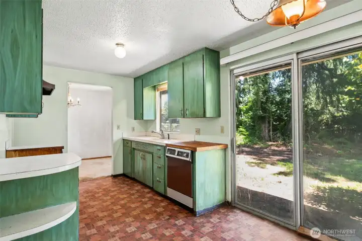 Natural light is definitely one of this kitchen's strong suits. The large sliding glass door draws sunlight deep into the space while providing peaceful views of the wooded backyard beyond, making the casual dining area feel bright and inviting throughout the day. Overhead hangs another fantastic vintage detail: a copper-toned lantern-style light fixture suspended from a chain that feels perfectly at home with the home's original character. Together with the vintage flooring and cabinetry, it creates a space that has managed to retain much of its mid-century personality. Natural light is definitely one of this kitchen's strong suits. The large sliding glass door draws sunlight deep into the space while providing peaceful views of the wooded backyard beyond, making the casual dining area feel bright and inviting throughout the day. Overhead hangs another fantastic vintage detail: a copper-toned lantern-style light fixture suspended from a chain that feels perfectly at home with the home's original character. Together with the vintage flooring and cabinetry, it creates a space that has managed to retain much of its mid-century personality.