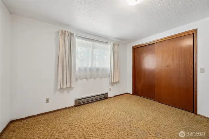 The largest of the three bedrooms, this spacious room measures approximately 12.5' x 10.5' and continues the home's wonderfully preserved mid-century character. One of the standout features here is the extra-wide closet doors, a design detail that feels distinctly of the era while providing excellent access to the closet space behind. Another original ceiling fixture remains in place, adding to the home's time-capsule appeal, while the window and curtains help soften the room with natural light throughout the day. The largest of the three bedrooms, this spacious room measures approximately 12.5' x 10.5' and continues the home's wonderfully preserved mid-century character. One of the standout features here is the extra-wide closet doors, a design detail that feels distinctly of the era while providing excellent access to the closet space behind. Another original ceiling fixture remains in place, adding to the home's time-capsule appeal, while the window and curtains help soften the room with natural light throughout the day.
