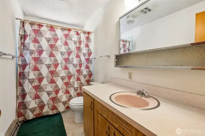 Between the original vanity, the vintage mirrored medicine cabinet and that fantastic blush-toned sink, it's easy to imagine this space looking much the same as it did decades ago. The long vanity countertop offers abundant storage and prep space, something many newer homes surprisingly lack. Natural light filters in through the window above the tub and shower area, helping the room feel open and bright throughout the day. For vintage enthusiasts, there are some fun original details worth preserving here. For renovators, the footprint is particularly appealing, with enough vanity space that a future double-sink setup could be a realistic possibility. Between the original vanity, the vintage mirrored medicine cabinet and that fantastic blush-toned sink, it's easy to imagine this space looking much the same as it did decades ago. The long vanity countertop offers abundant storage and prep space, something many newer homes surprisingly lack. Natural light filters in through the window above the tub and shower area, helping the room feel open and bright throughout the day. For vintage enthusiasts, there are some fun original details worth preserving here. For renovators, the footprint is particularly appealing, with enough vanity space that a future double-sink setup could be a realistic possibility.