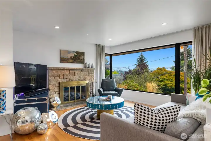Cozy fireplace anchors the living room with the huge picture window inviting the views. Custom drapery from The Shade Store.