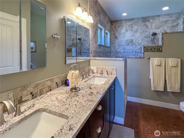 Beautiful primary bathroom with ceramic tile floors, double undermount sinks, granite counters and view of tiled shower complete with radiant in floor heat.