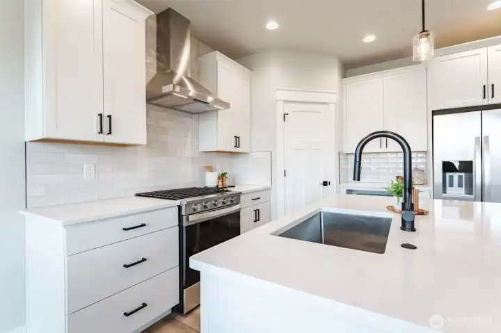 Quartz counters, gas range, stainless hood, and deep single-basin sink create a clean, modern workspace for home cooks.