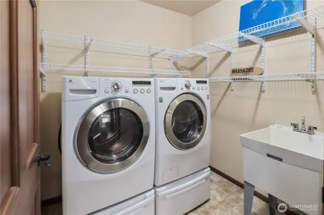 The dedicated laundry room is spacious and well-equipped, featuring a deep sink, ample shelving for storage, and plenty of room for folding and organizing.