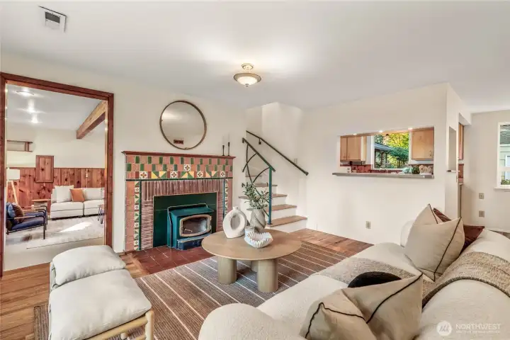 At the center of the home, the living room features original hardwood floors and a cozy wood-burning fireplace. The family room is to the left, kitchen to the right, with stairs leading up to the primary suite.