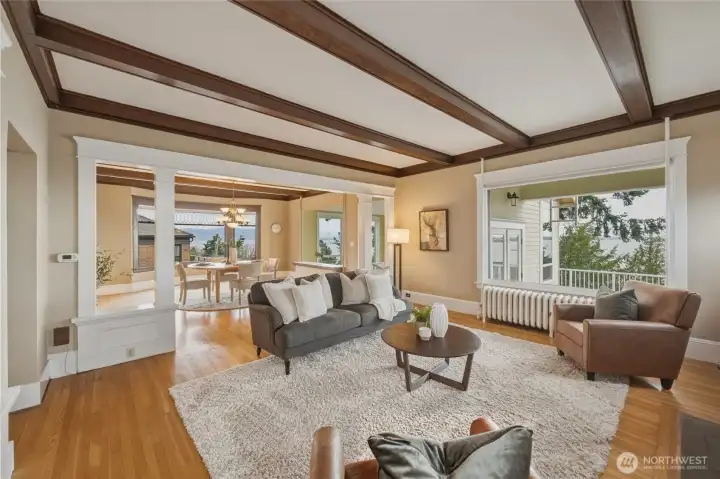 Stunning living room with original box-beam ceilings, hardwood floors, and open flow to the dining room.