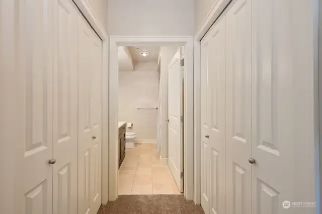 Dual closets and looking into the primary full bath with stone tiles.