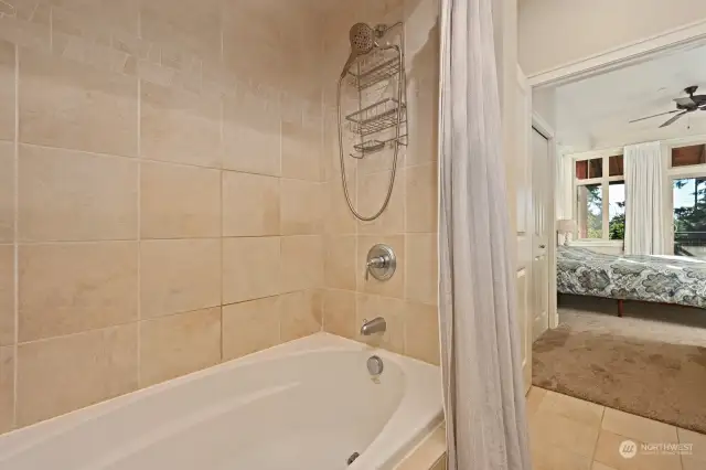 Oval shaped bath tub with shower combined, surrounds by nice stone tilework.