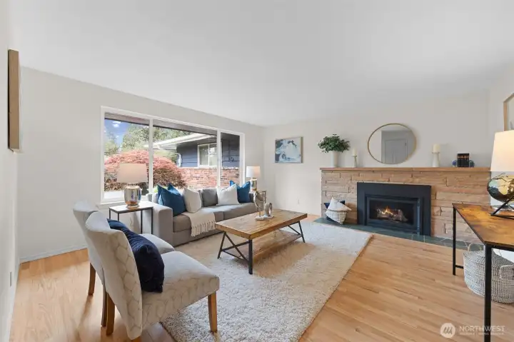 Warm and inviting living room with classic brick fireplace and large picture window. Refinished hardwoods and fresh paint create a bright, move-in ready feel with room to personalize.