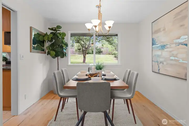 Bright dining area with a large window framing views of the backyard and mature landscaping. Positioned next to the kitchen for a seamless setup when hosting.