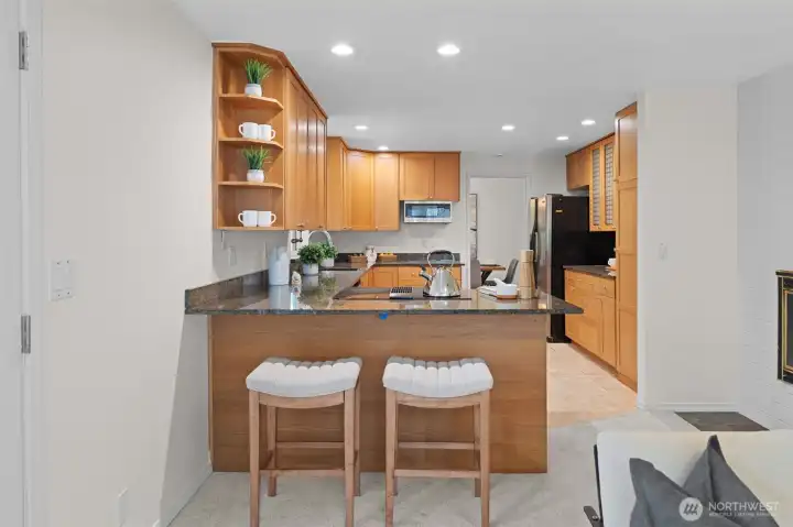 Kitchen with peninsula seating for two, granite countertops, and open shelving for display. Seamless connection to the living space creates an ideal setup for gathering and everyday living.