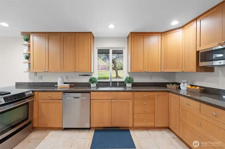 Expansive kitchen layout with abundant cabinetry, granite counters, and stainless steel appliances. Large window above the sink frames backyard views and brings natural light into the kitchen.