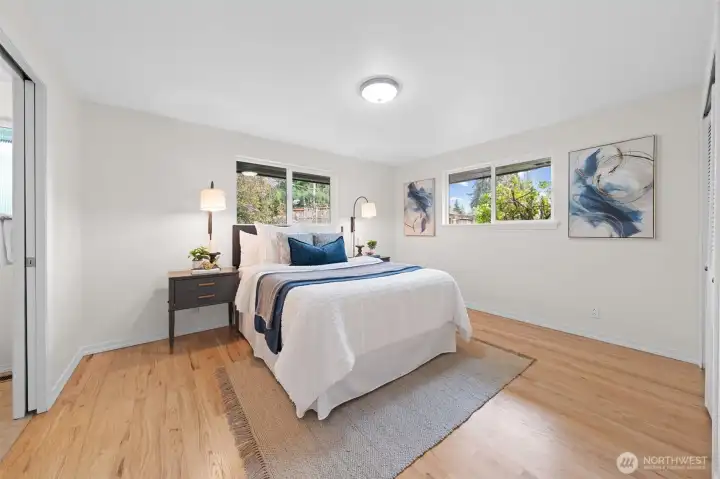 Primary Suite with wide layout, wood flooring, and multiple windows bringing in natural light and backyard views. Spacious design offers flexibility for additional seating or a workspace.