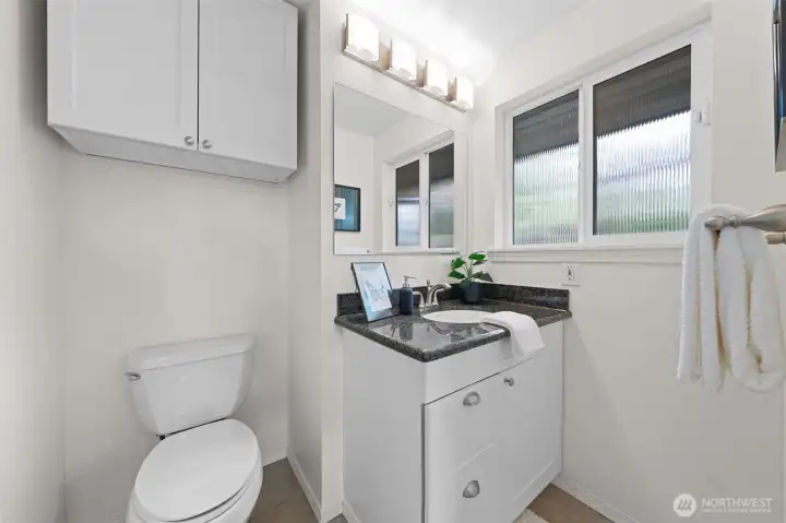 Primary Bath with granite countertop vanity, overhead storage, and a large mirror for added functionality. Window brings in natural light while maintaining privacy.