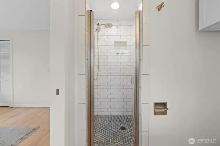 Walk-in shower with tile surround, glass enclosure, and built-in niche for storage. Clean design with updated finishes creates a streamlined, modern look.