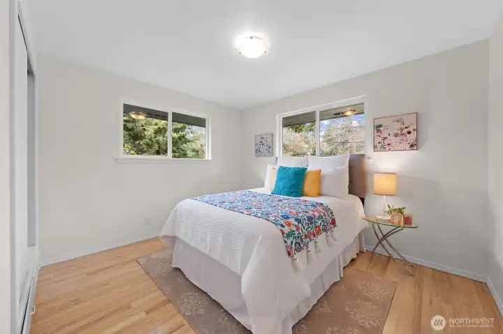 Bedroom two features dual windows bringing in natural light and views of surrounding greenery. Functional layout with wood flooring offers flexibility for guest space or everyday use.