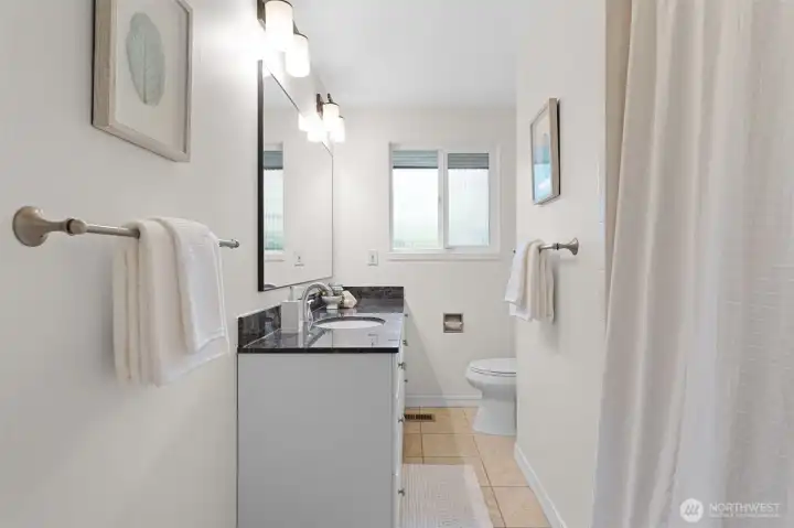 Full bath with granite countertop vanity, extended mirror, and updated lighting. Tub and shower combination with clean finishes and a window for added light.