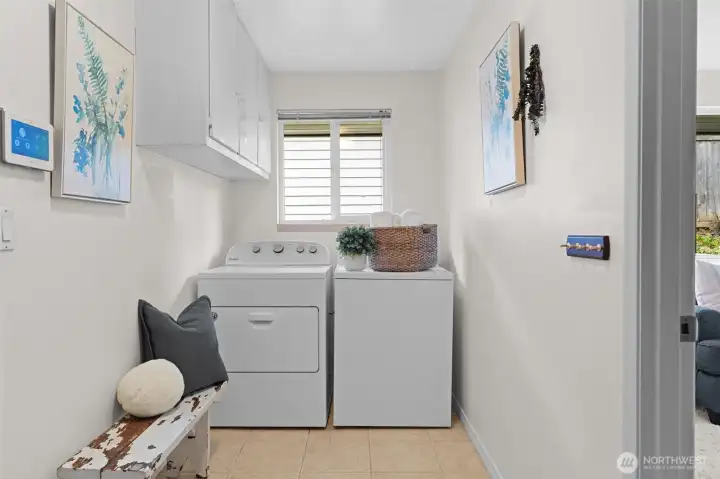 Utility room with side-by-side washer and dryer, overhead cabinetry, and a window for natural light. Functional layout with built-in seating and storage keeps everyday tasks organized and efficient.