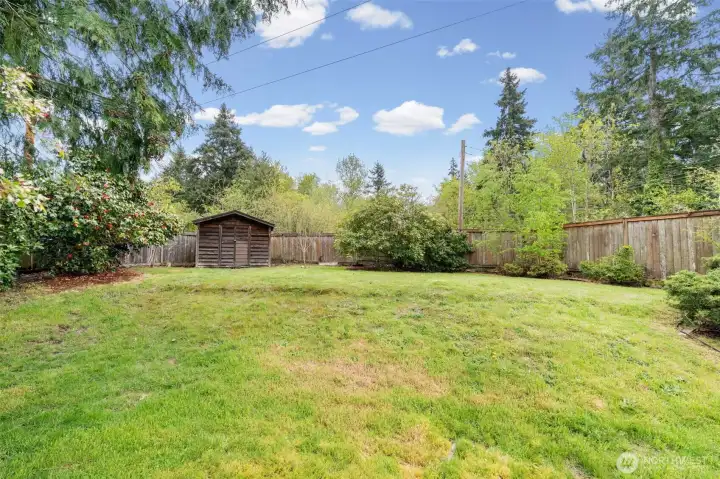 Large backyard with storage shed, perimeter fencing, and established landscaping. Level lawn provides flexibility for entertaining, recreation, or relaxing outdoors.