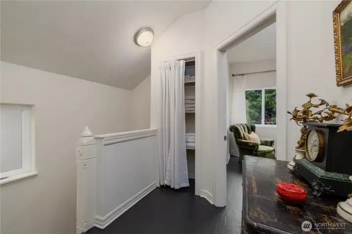Quaint Newel post at the spacious landing on the top of the stairs, vaulted ceiling, stairway window, painted wood floors and convenient linen closet.